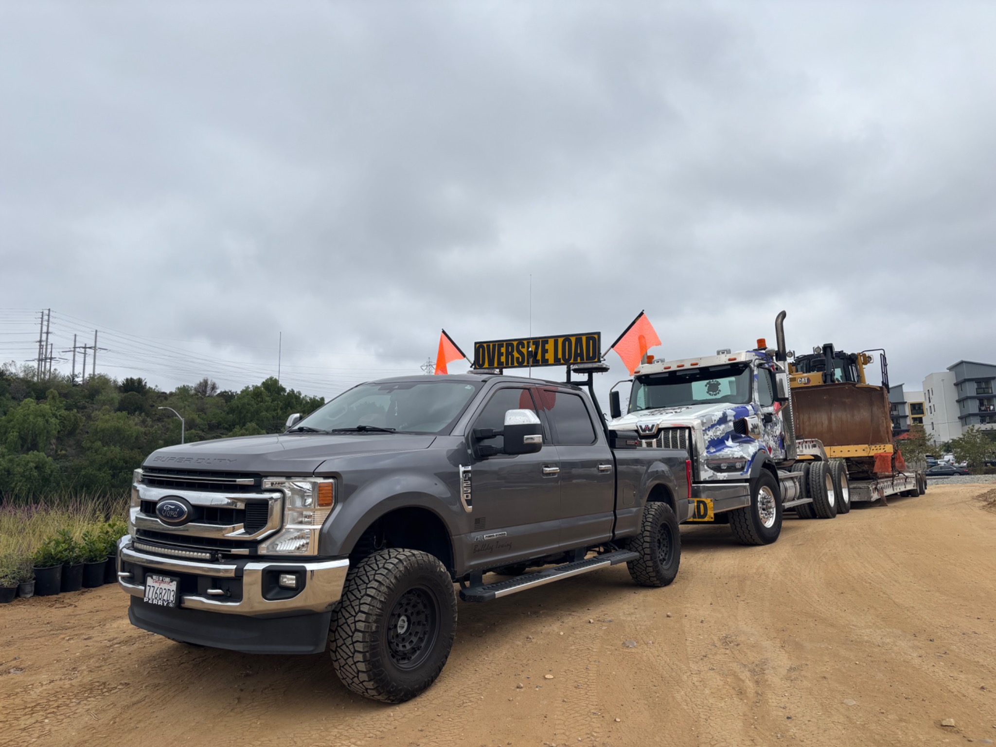 Pilot car escort vehicle staged with oversize load and heavy equipment.