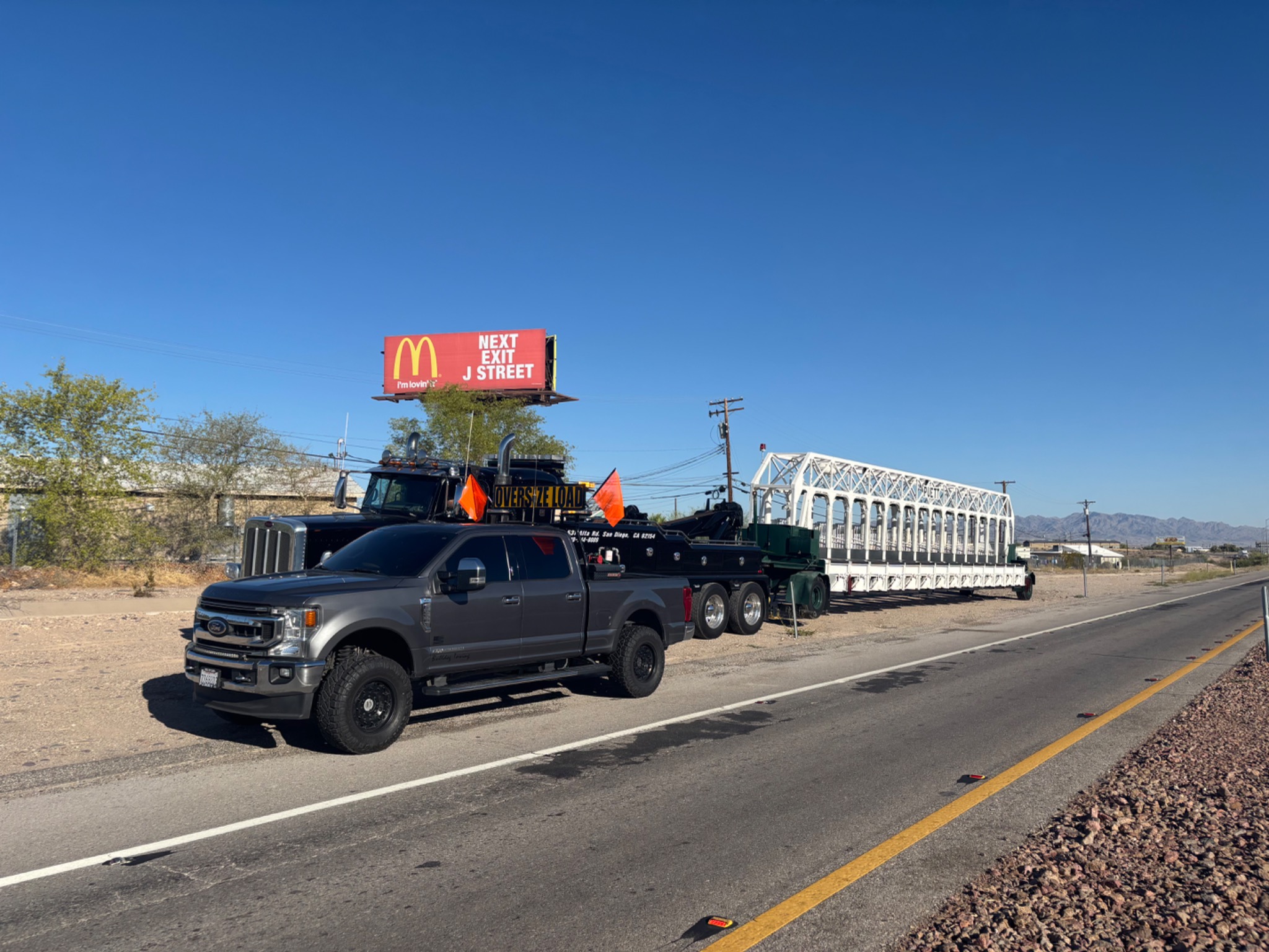 Pilot car escort vehicle supporting transport of a large truss structure on highway.